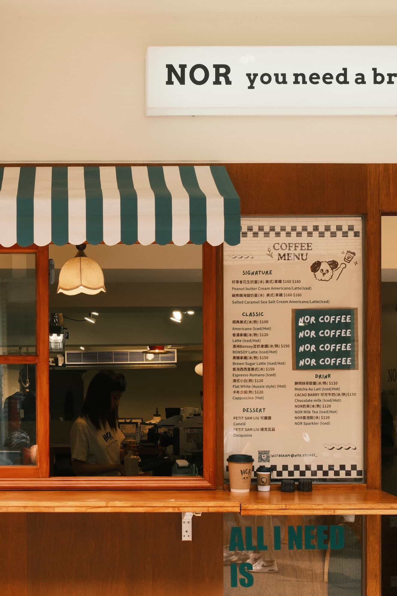 NOR Coffee’s window counter on Lane 53: “NOR you need a break” sign, striped awning, the coffee menu board and a barista at work